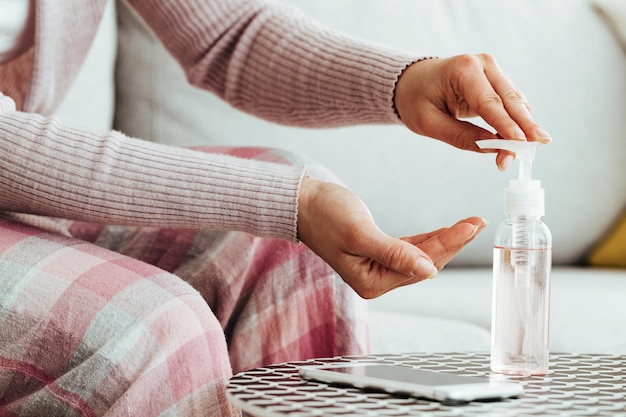 Primo piano della donna che usa il dispenser di gel igienizzante mentre si pulisce le mani a casa