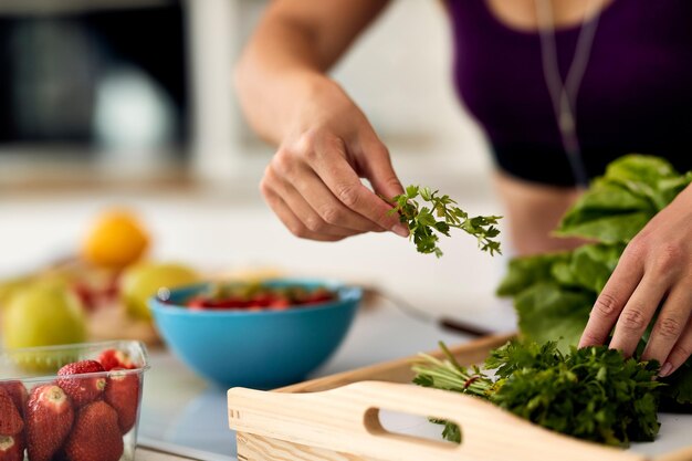 Primo piano della donna che usa il prezzemolo mentre prepara il cibo sano in cucina