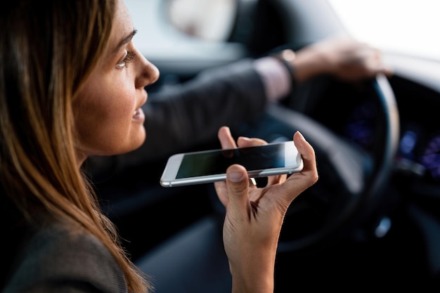 Primo piano della donna che utilizza il telefono cellulare e parla sull'altoparlante mentre si guida l'auto