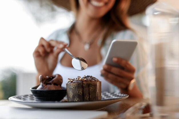 Primo piano della donna che utilizza lo smartphone mentre si mangia la torta in un caffè Il fuoco è in primo piano