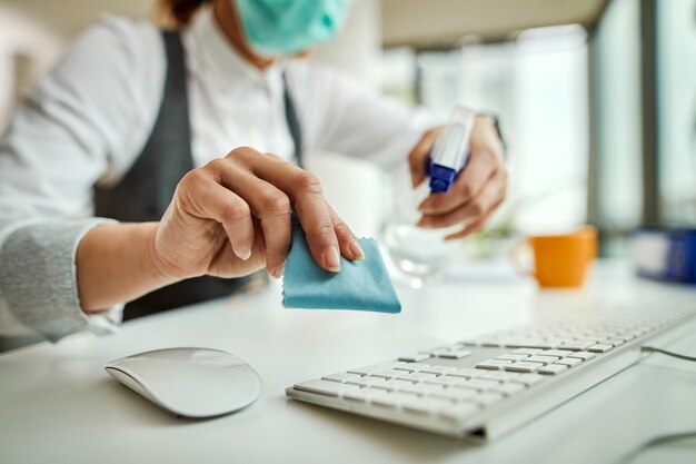 Primo piano della donna d'affari che disinfetta la tastiera del computer in ufficio