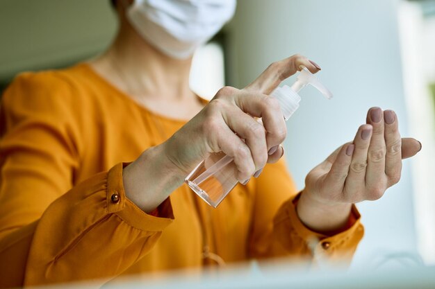 Primo piano della donna d'affari che utilizza un disinfettante per le mani mentre si lavora in ufficio