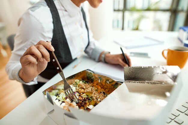 Primo piano della donna di affari che mangia un pasto sano mentre lavora nell'ufficio