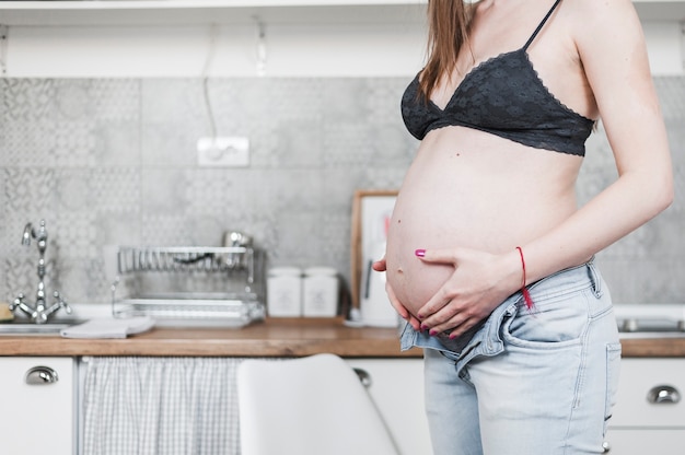 Primo piano della donna incinta che sta vicino al contatore di cucina che tiene la sua pancia