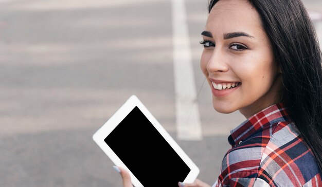 Primo piano della donna sorridente che esamina macchina fotografica mentre per mezzo della compressa digitale sulla via