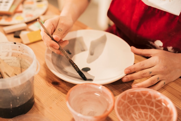 Primo piano della femmina che dipinge le stoviglie con il pennello sulla tavola di legno