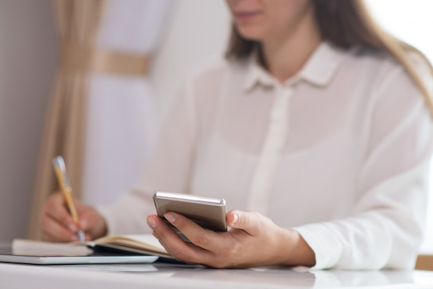 Primo piano della giovane donna che si siede al telefono cellulare della tenuta della tavola