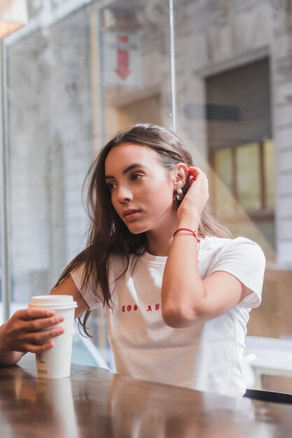 Primo piano della giovane donna che si siede in caffè che tiene la tazza di caffè a disposizione