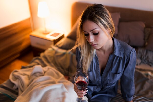 Primo piano della giovane donna che si siede sul letto che tiene bicchiere di vino