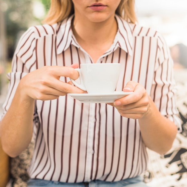 Primo piano della giovane donna che tiene tazza bianca e piattino