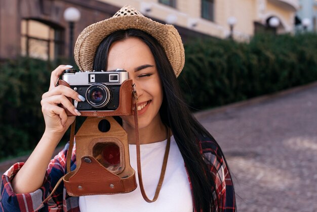 Primo piano della giovane donna felice che prende foto con la macchina fotografica ad all'aperto