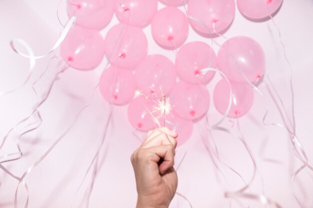 Primo piano della mano che tiene sparkler illuminato sotto il soffitto decorativo con palloncini rosa