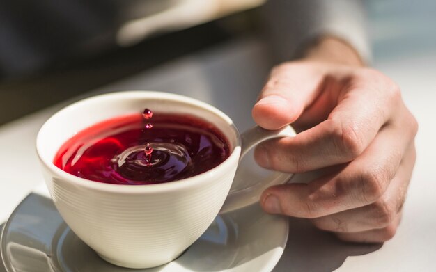 Primo piano della mano che tiene una tazza della tazza di tè rossa appena prodotta