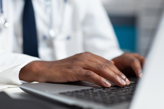 Primo piano della mano del medico afroamericano digitando prescrizione medica dopo aver analizzato le competenze di malattia del paziente. Uomo del terapista che lavora al trattamento sanitario nell'ufficio dell'ospedale. Servizio di medicina