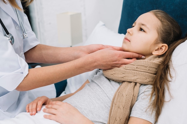 Primo piano della mano del medico della femmina che controlla la gola e il collo del paziente della ragazza