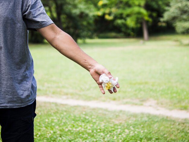 Primo piano della mano dell'uomo che getta carta sgualcita in parco