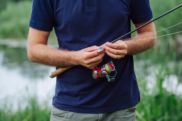 Primo piano della mano dell&#39;uomo che lega il gancio di pesca sulla canna da pesca