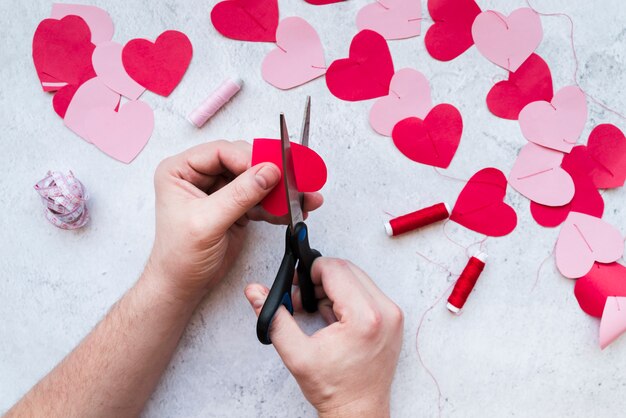 Primo piano della mano dell&#39;uomo che rende la ghirlanda di forma cuore su sfondo bianco strutturato