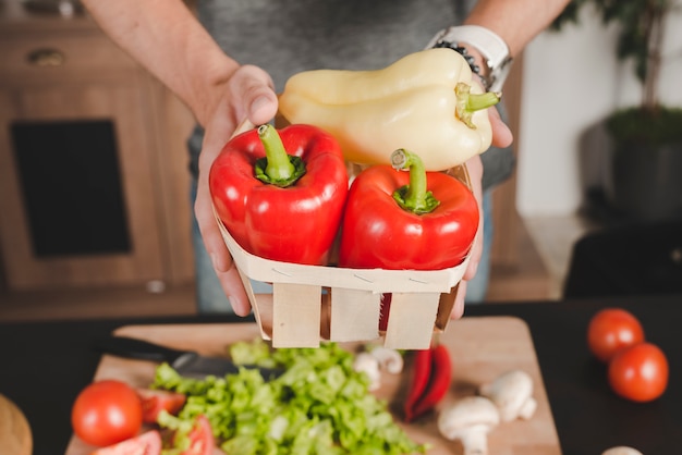 Primo piano della mano dell&#39;uomo che tiene il bellpepper rosso e giallo nel cestino