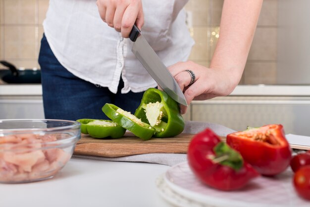 Primo piano della mano della donna che taglia il peperone dolce con il coltello tagliente sul tagliere