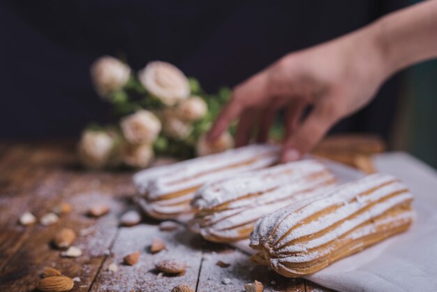 Primo piano della mano della donna che tiene eclairs al forno con le mandorle sulla tavola di legno