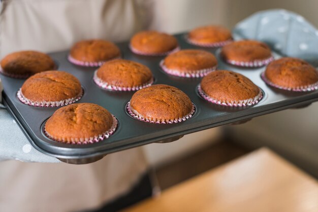 Primo piano della mano della donna che tiene i muffin al forno nel vassoio di cottura