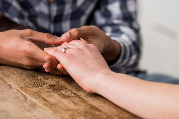 Primo piano della mano della holding del giovane della sua amica sullo scrittorio di legno