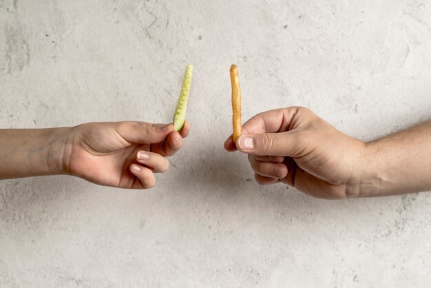 Primo piano della mano della persona che tiene fetta di cetriolo e patatine fritte su sfondo concreto