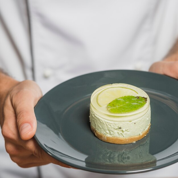 Primo piano della mano dello chef che tiene delizioso dessert sul piatto riflettente