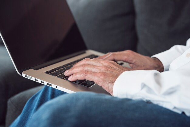Primo piano della mano di un uomo anziano che digita sul computer portatile
