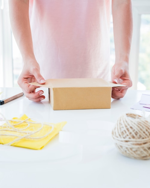 Primo piano della mano di una donna che avvolge il contenitore di regalo sulla tavola bianca