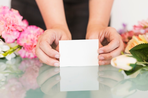 Primo piano della mano di una donna che tiene il biglietto da visita bianco in bianco sopra lo scrittorio