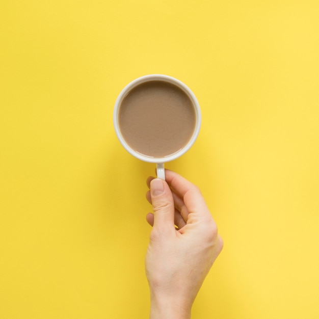 Primo piano della mano di una persona che tiene tazza di caffè su sfondo giallo