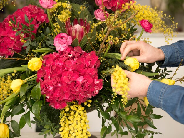 Primo piano della mano maschio del fiorista che sistema i fiori nel vaso
