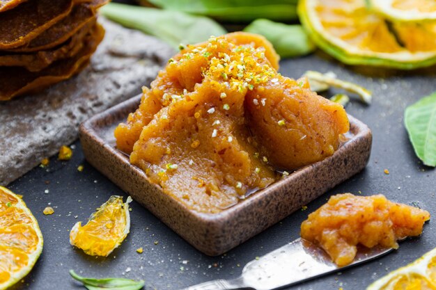 Primo piano della marmellata di mandarini in un piatto su un tavolo circondato da foglie e mandarini secchi