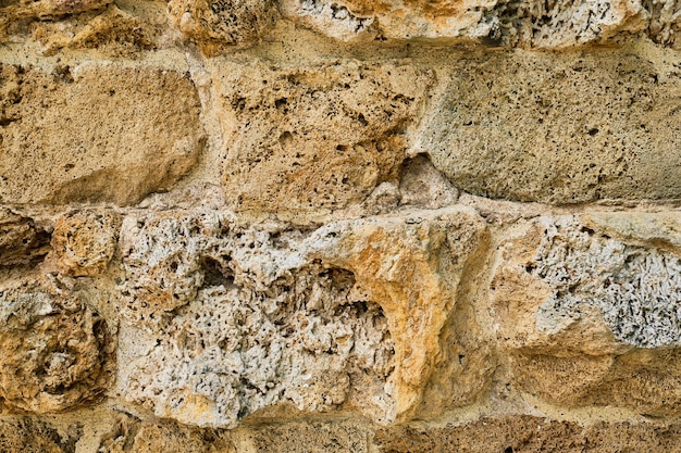 Primo piano della muratura di un antico muro di arenaria morbida che è stato eroso dall'idea di pietra naturale del tempo per lo sfondo o l'interno