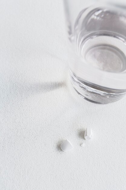 Primo piano della pillola bianca rotta con bicchiere d&#39;acqua