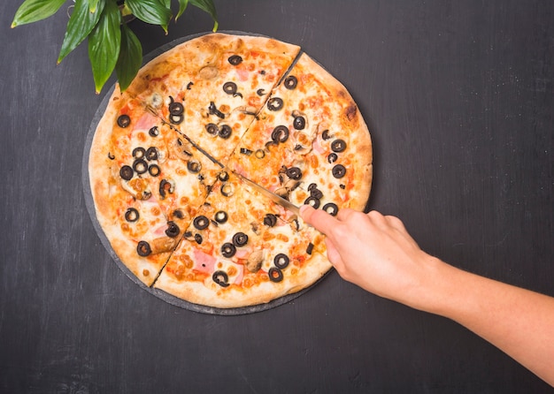 Primo piano della pizza di taglio a mano con un coltello affilato