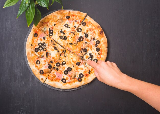 Primo piano della pizza di taglio a mano con un coltello affilato