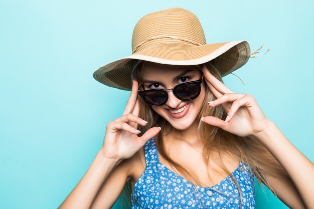 Primo piano della ragazza abbastanza gioiosa in cappello di paglia pronto per il viaggio in posa in studio su sfondo blu.