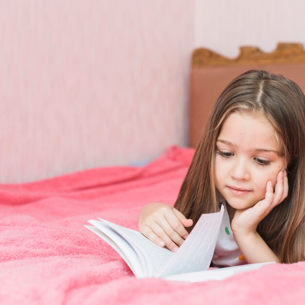 Primo piano della ragazza che si trova sul libro di lettura del letto