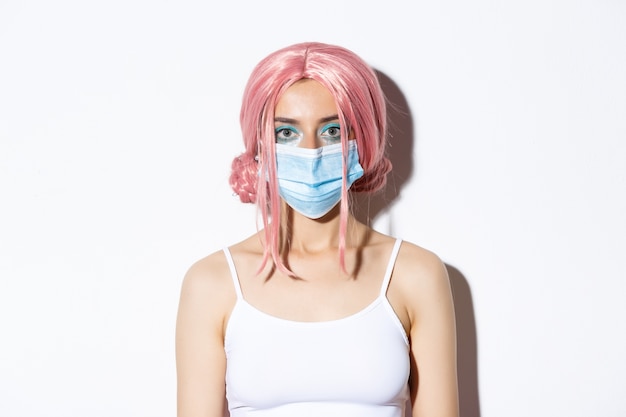 Primo piano della ragazza con parrucca rosa e maschera medica, che celebra Halloween durante la pandemia di coronavirus, in piedi.