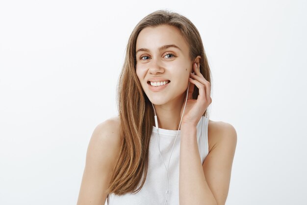 Primo piano della ragazza sorridente che indossa gli auricolari, ascolta musica o podcast lungo la strada