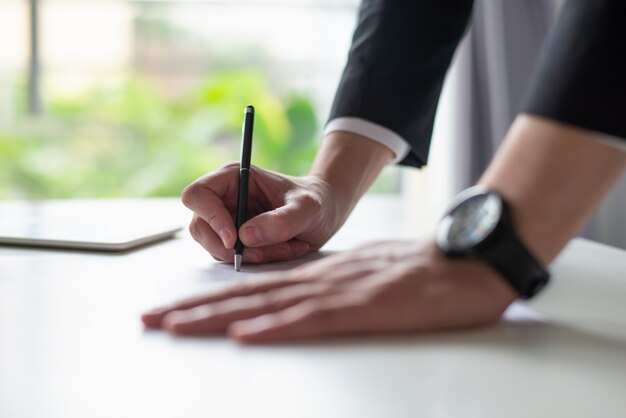 Primo piano della scrittura dell&#39;uomo di affari sul foglio di carta allo scrittorio