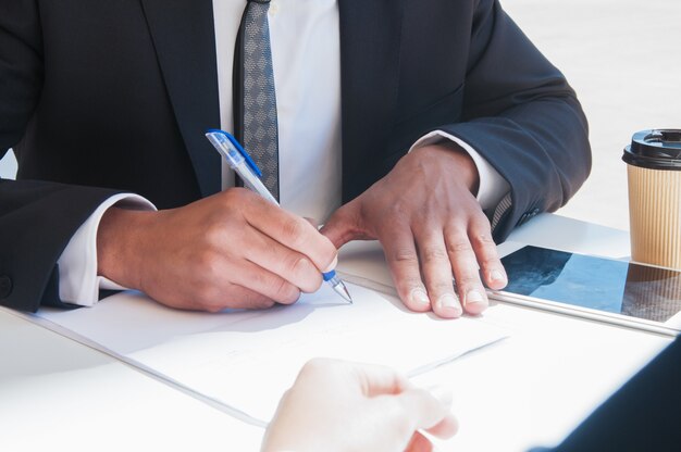 Primo piano della scrittura dell&#39;uomo di affari sullo strato di carta alla tavola