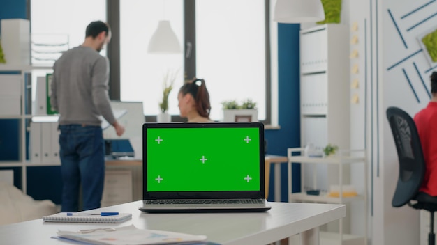 Primo piano della scrivania vuota con schermo verde sul computer portatile nell'ufficio di avvio. Computer con modello isolato, sfondo chiave di crominanza e mock up vuoto nello spazio aziendale. Copia spazio chromakey