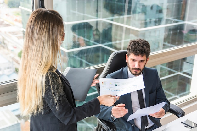 Primo piano della segretaria femminile che dà rapporto finanziario al responsabile maschio sul posto di lavoro