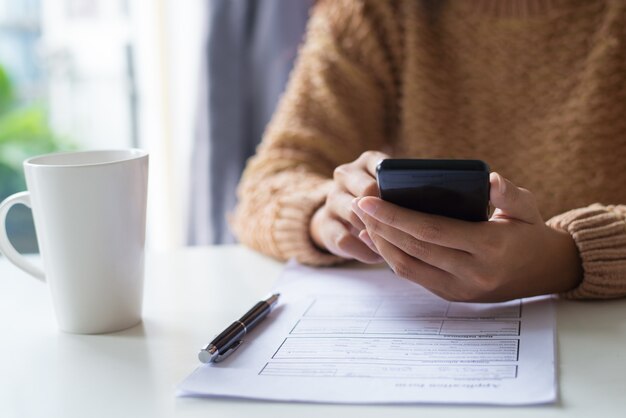 Primo piano della signora di affari che utilizza dispositivo mentre esaminando documento