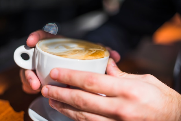 Primo piano della tazza di caffè di arte del latte della tenuta della mano di una persona