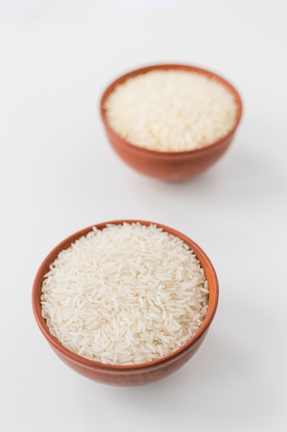 Primo piano delle ciotole di riso gelsomino crudo su carta da parati bianca